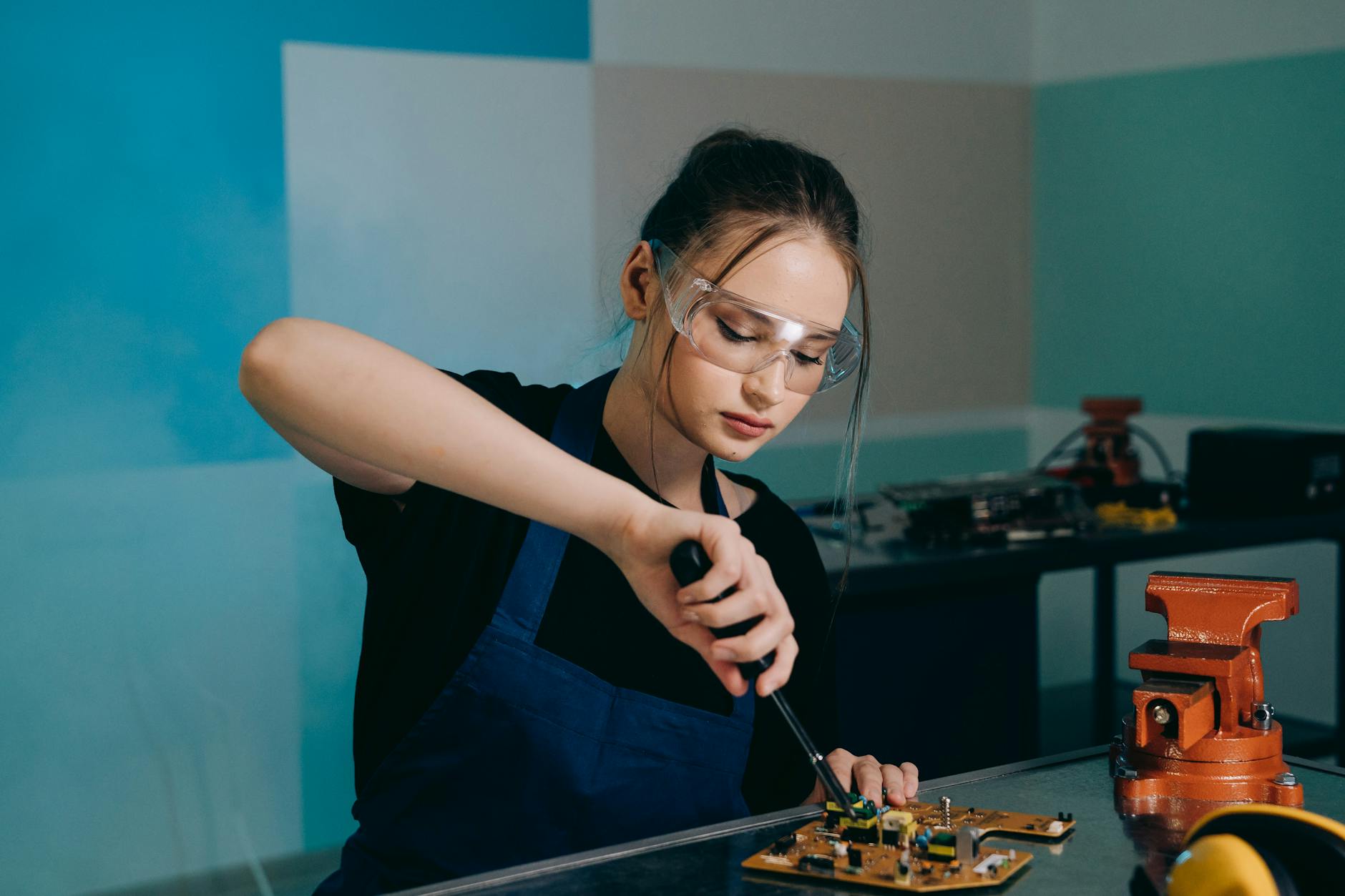 woman holding a soldering iron while wearing protective goggles